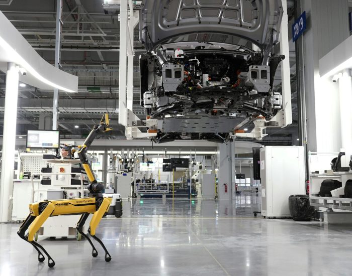 A robotic dog oversees an automated car assembly in a high-tech factory setting.