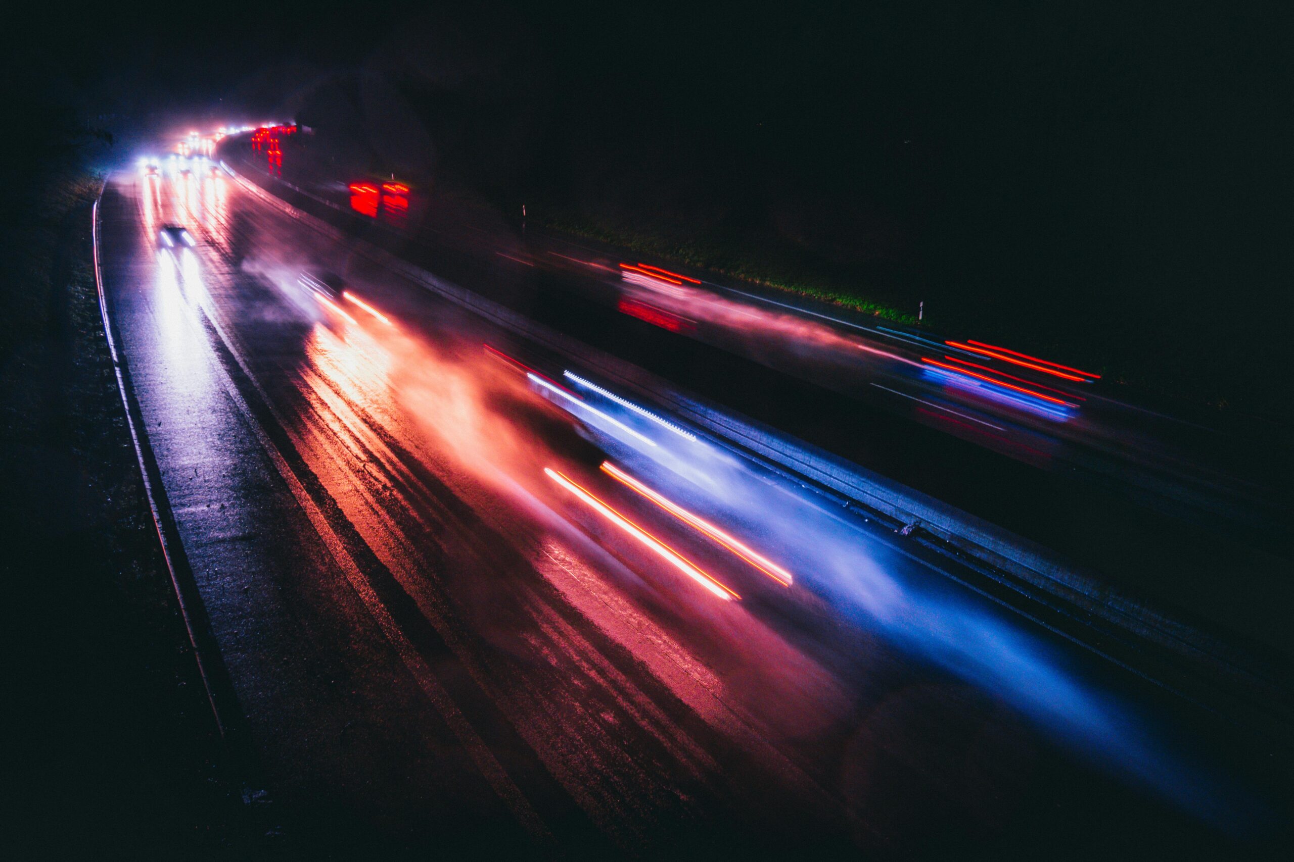 Long exposure photo capturing vibrant light trails on a rainy highway night.
