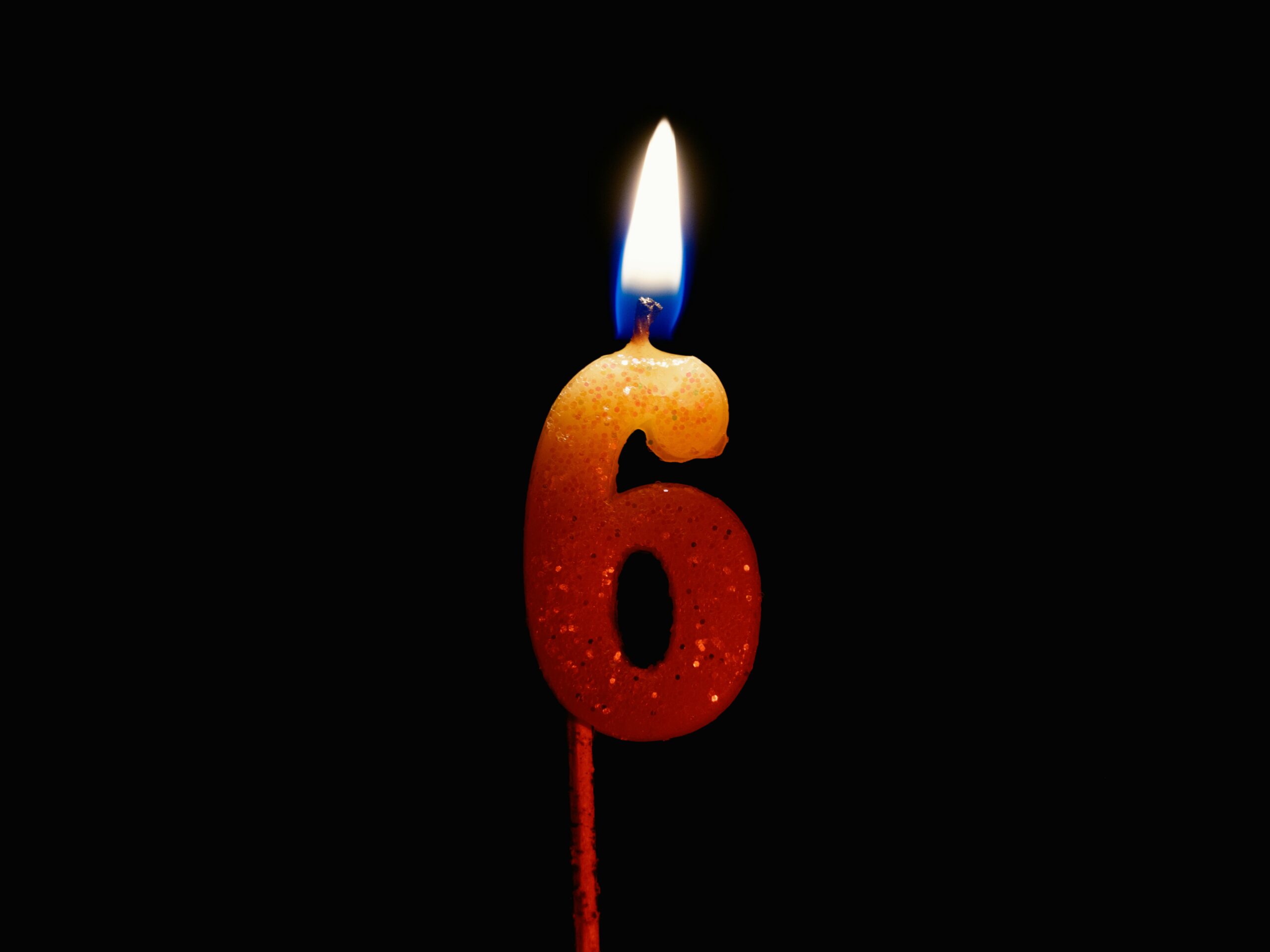 Close-up of a number six birthday candle burning brightly against a dark background.